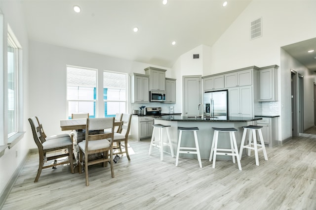 kitchen featuring backsplash, appliances with stainless steel finishes, light hardwood / wood-style floors, and a kitchen bar