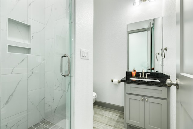 bathroom featuring vanity, hardwood / wood-style flooring, toilet, and a shower with shower door