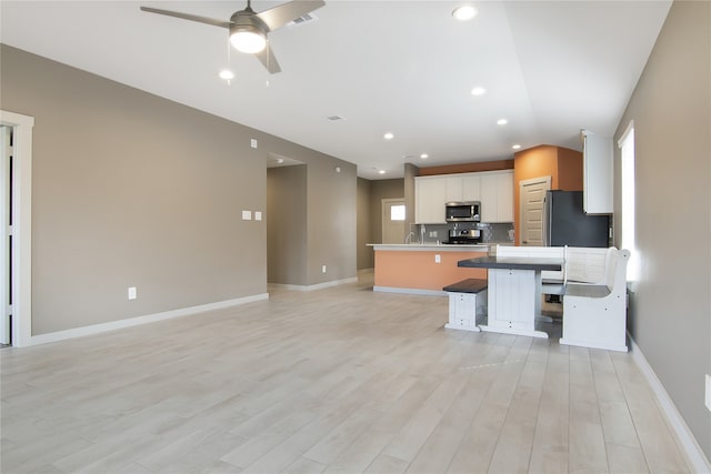 kitchen with appliances with stainless steel finishes, white cabinetry, a breakfast bar, kitchen peninsula, and ceiling fan