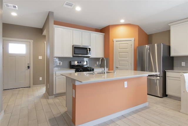 kitchen with white cabinets, an island with sink, stainless steel appliances, and tasteful backsplash