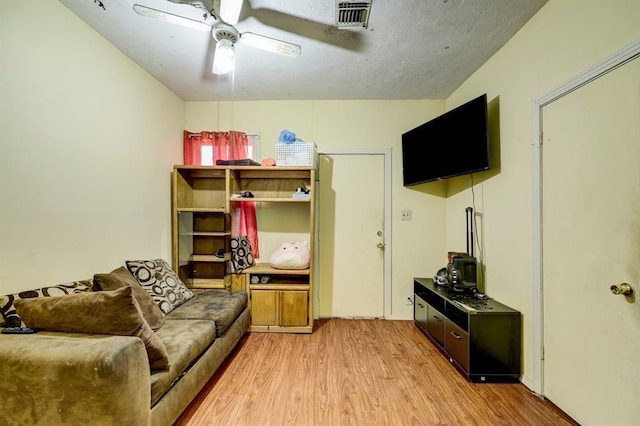 living room featuring ceiling fan, a textured ceiling, and light hardwood / wood-style flooring