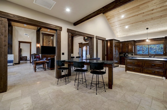 kitchen featuring beam ceiling, high vaulted ceiling, dark brown cabinetry, a kitchen bar, and wooden ceiling