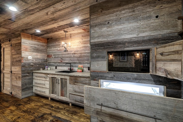 bar with wood walls, sink, hanging light fixtures, wood ceiling, and dark wood-type flooring