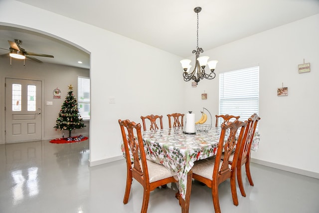 dining area featuring ceiling fan with notable chandelier and concrete floors