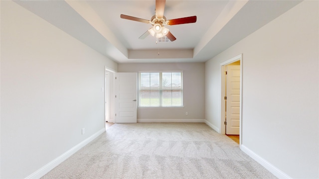 carpeted spare room with a tray ceiling and ceiling fan