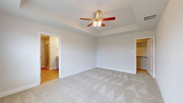 unfurnished bedroom featuring connected bathroom, a walk in closet, a raised ceiling, light carpet, and a closet