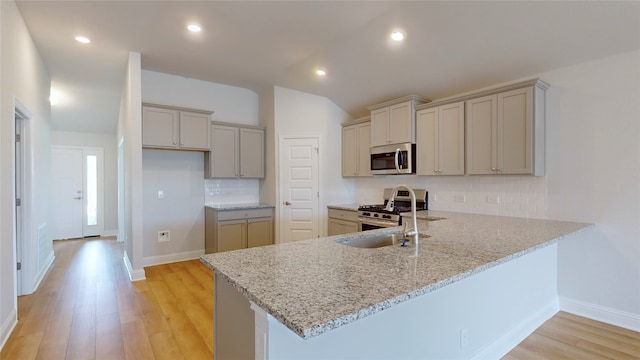 kitchen with light hardwood / wood-style flooring, light stone counters, backsplash, and stainless steel appliances