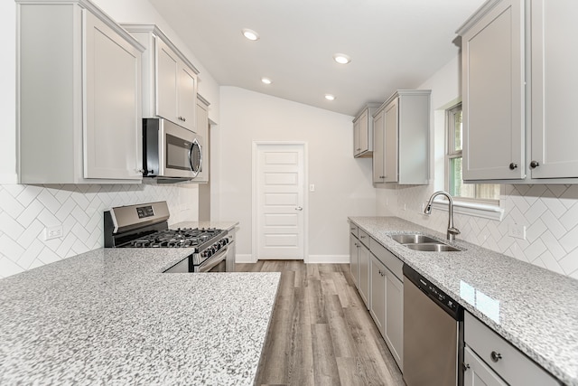 kitchen featuring vaulted ceiling, light wood-type flooring, backsplash, and appliances with stainless steel finishes