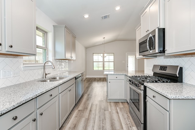 kitchen with decorative light fixtures, backsplash, light wood-type flooring, appliances with stainless steel finishes, and sink