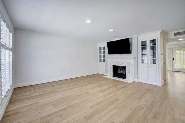 unfurnished living room featuring built in shelves, light wood-type flooring, and a high end fireplace