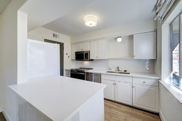 kitchen featuring stainless steel appliances, decorative backsplash, white cabinets, light wood-type flooring, and kitchen peninsula