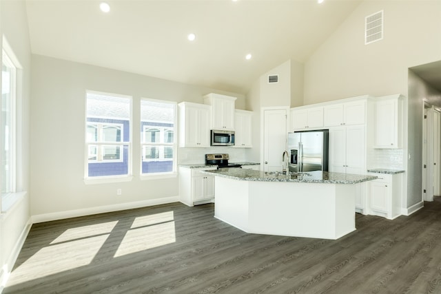 kitchen featuring appliances with stainless steel finishes, white cabinets, a center island with sink, and light stone countertops