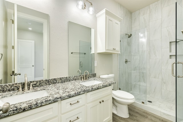 bathroom featuring wood-type flooring, a shower with door, large vanity, dual sinks, and toilet