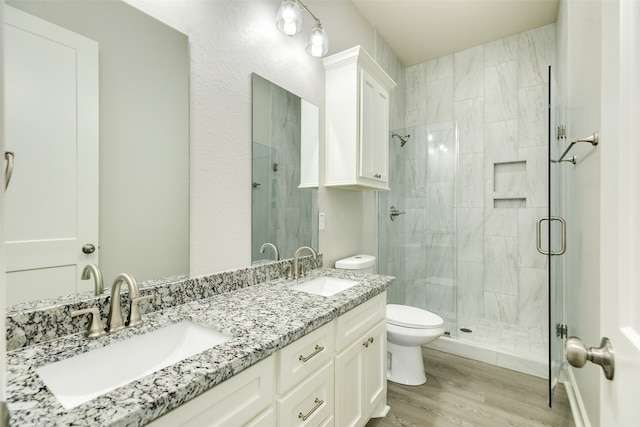 bathroom featuring vanity with extensive cabinet space, a shower with door, double sink, hardwood / wood-style flooring, and toilet