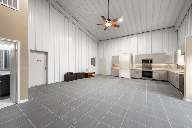 unfurnished living room featuring sink, tile patterned floors, ceiling fan, and a high ceiling