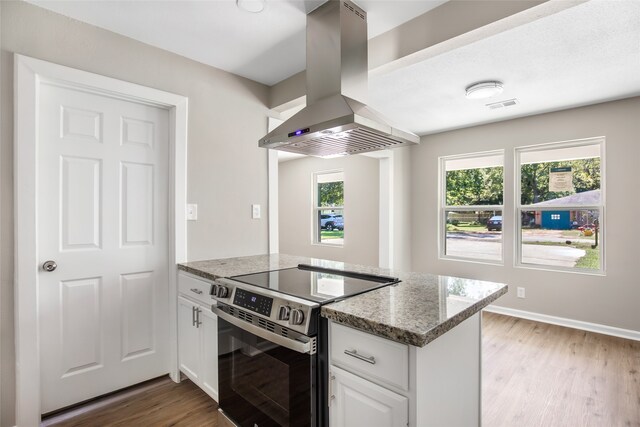 kitchen with wall chimney range hood, white cabinetry, plenty of natural light, and electric stove