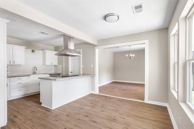 kitchen with white cabinetry, kitchen peninsula, wall chimney exhaust hood, and light wood-type flooring