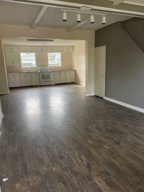 unfurnished living room featuring wood walls, beamed ceiling, dark hardwood / wood-style floors, and sink