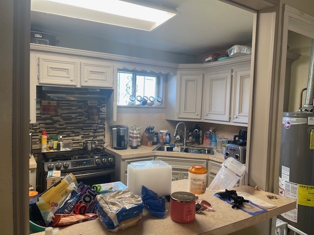 kitchen featuring backsplash, gas stove, sink, water heater, and white cabinets