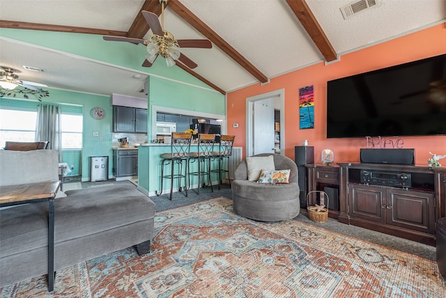 carpeted living room featuring vaulted ceiling with beams, ceiling fan, and a textured ceiling