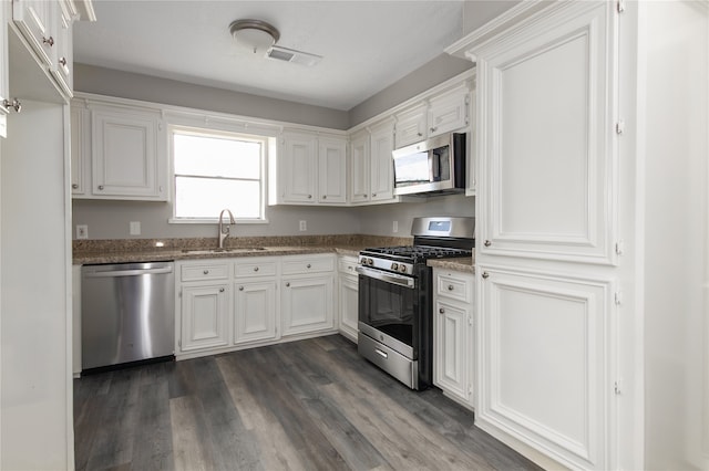 kitchen featuring appliances with stainless steel finishes, white cabinets, sink, dark hardwood / wood-style floors, and dark stone countertops