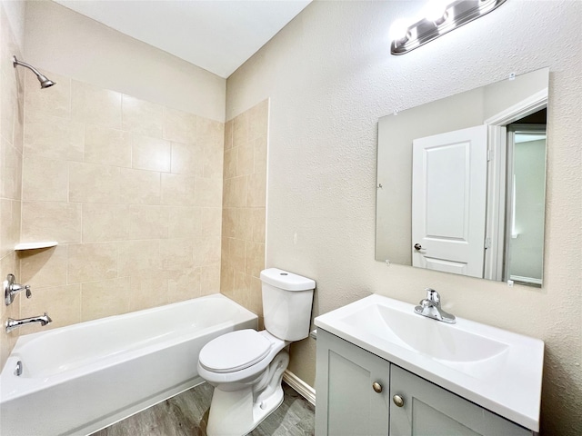 bathroom featuring toilet, wood finished floors, shower / bathtub combination, a textured wall, and vanity