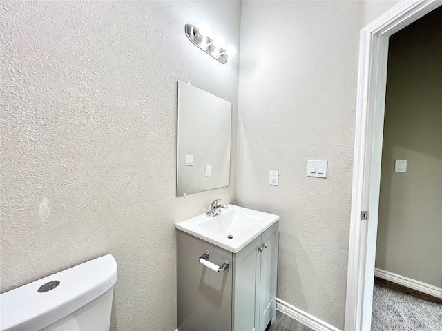 half bath featuring baseboards, toilet, vanity, and a textured wall