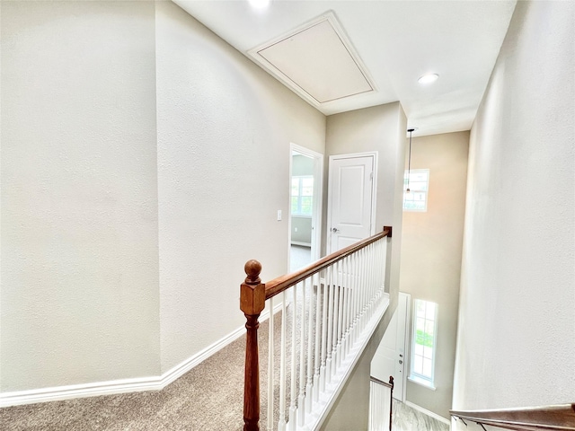 hall featuring an upstairs landing, attic access, baseboards, and carpet floors