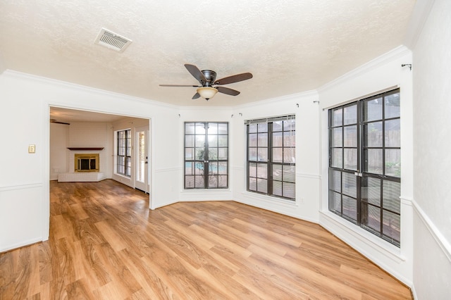 unfurnished room featuring a brick fireplace, crown molding, light hardwood / wood-style floors, and a textured ceiling