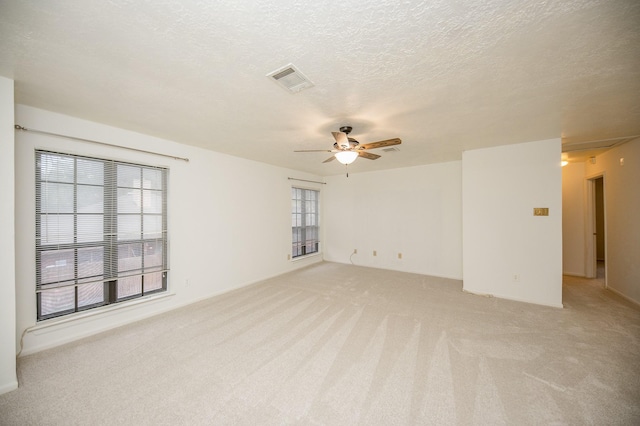 spare room featuring ceiling fan, a healthy amount of sunlight, light colored carpet, and a textured ceiling