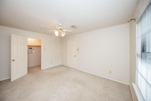 unfurnished bedroom featuring light carpet, a spacious closet, a closet, and ceiling fan