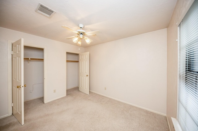 unfurnished bedroom with multiple closets, light colored carpet, and ceiling fan