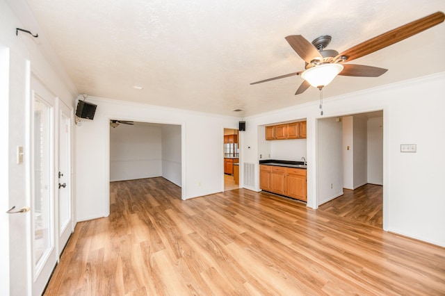 unfurnished living room with a textured ceiling, light hardwood / wood-style flooring, ornamental molding, and ceiling fan