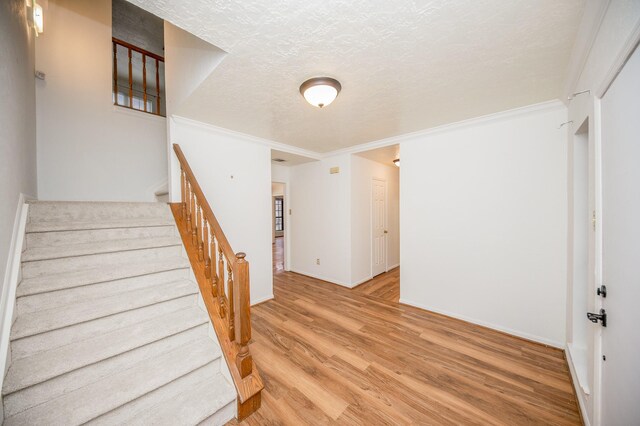 stairs with crown molding, hardwood / wood-style floors, and a textured ceiling