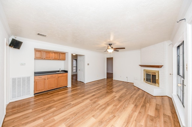 unfurnished living room featuring crown molding, a brick fireplace, light hardwood / wood-style flooring, and a textured ceiling