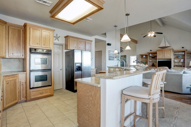 kitchen with beam ceiling, stainless steel appliances, a kitchen breakfast bar, pendant lighting, and a center island with sink