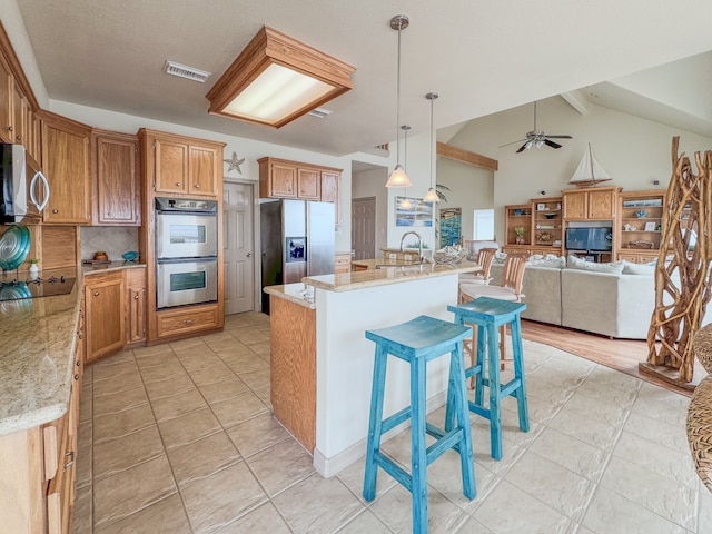 kitchen with appliances with stainless steel finishes, decorative light fixtures, vaulted ceiling with beams, a breakfast bar area, and an island with sink