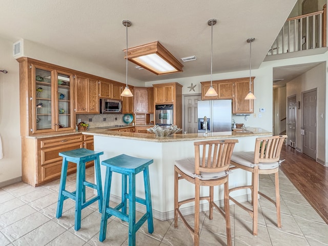 kitchen with pendant lighting, backsplash, stainless steel appliances, and light hardwood / wood-style floors