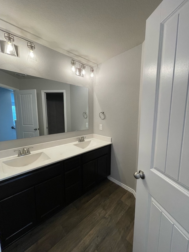 bathroom featuring wood-type flooring, a textured ceiling, and dual bowl vanity