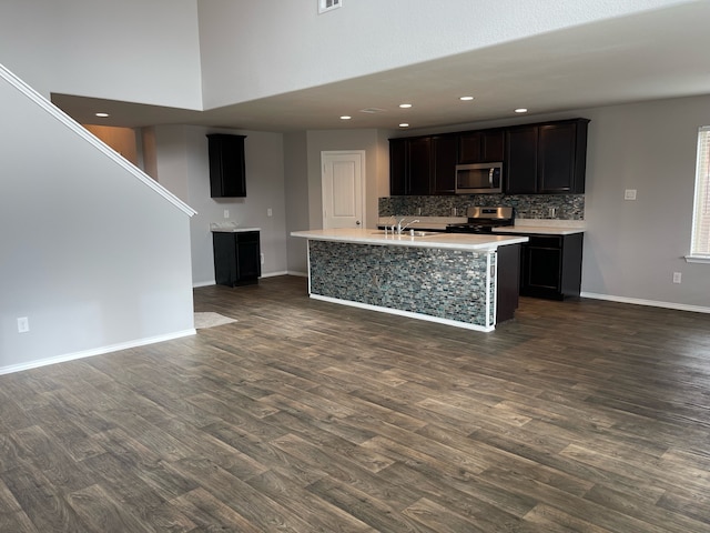 kitchen with decorative backsplash, sink, dark wood-type flooring, appliances with stainless steel finishes, and a kitchen island with sink