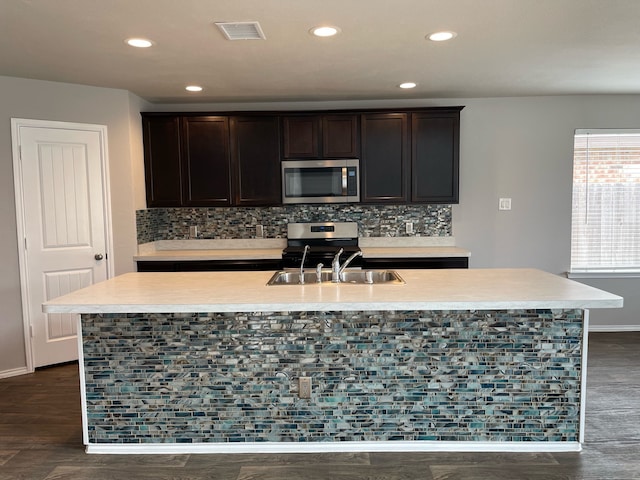 kitchen with dark hardwood / wood-style floors, tasteful backsplash, a kitchen island with sink, and appliances with stainless steel finishes