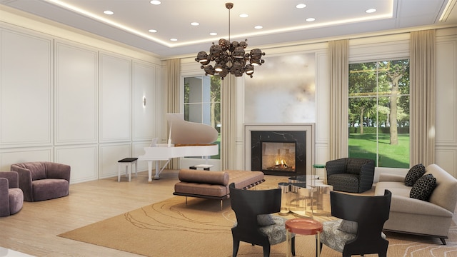 living room with light wood-type flooring, a tray ceiling, a chandelier, and a premium fireplace