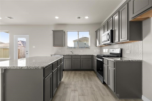 kitchen with stainless steel appliances, gray cabinetry, backsplash, light stone countertops, and light wood-type flooring