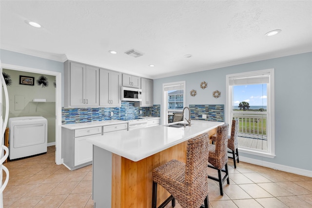 kitchen with washer / clothes dryer, tasteful backsplash, sink, a kitchen island with sink, and white appliances