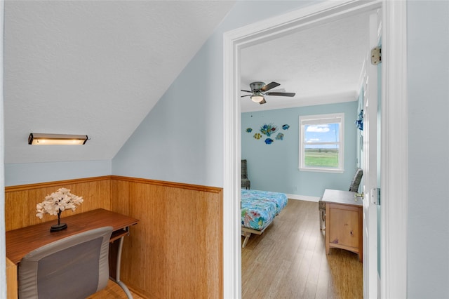 bedroom featuring ceiling fan, lofted ceiling, light wood-type flooring, and wood walls