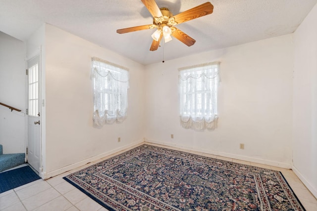 empty room with ceiling fan, light tile patterned flooring, and a textured ceiling