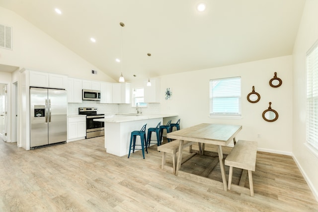 kitchen with pendant lighting, light hardwood / wood-style flooring, backsplash, kitchen peninsula, and stainless steel appliances