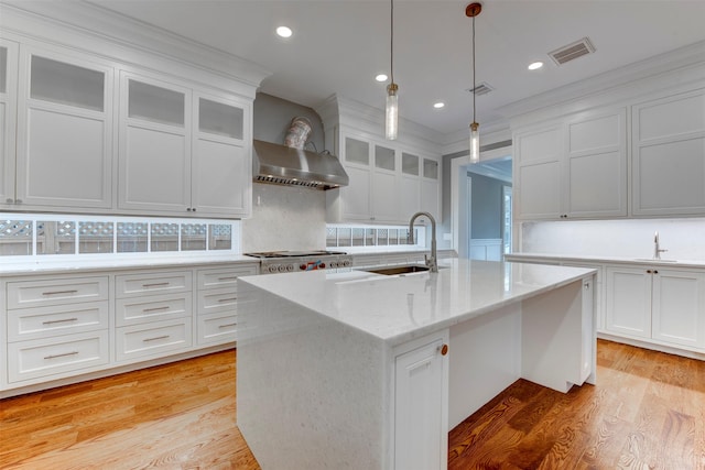 kitchen featuring white cabinetry, wall chimney exhaust hood, light stone countertops, and a kitchen island with sink