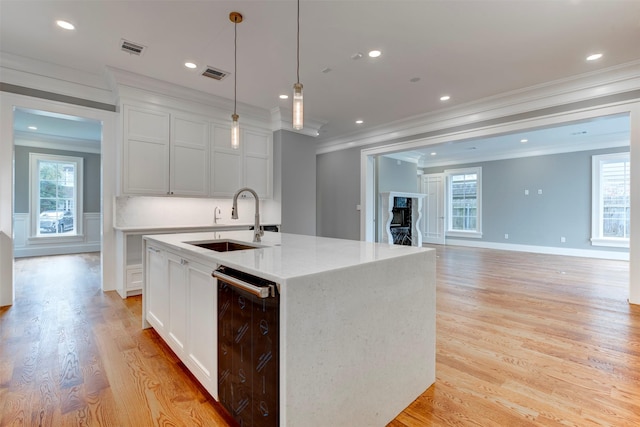 kitchen with sink, decorative light fixtures, an island with sink, and white cabinets