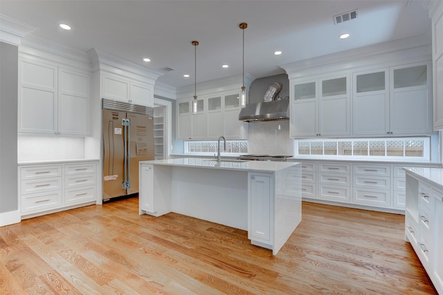 kitchen featuring sink, hanging light fixtures, stainless steel built in fridge, a center island with sink, and wall chimney range hood